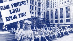 A woman holds a sign reading "Equal Positions with Equal Pay"