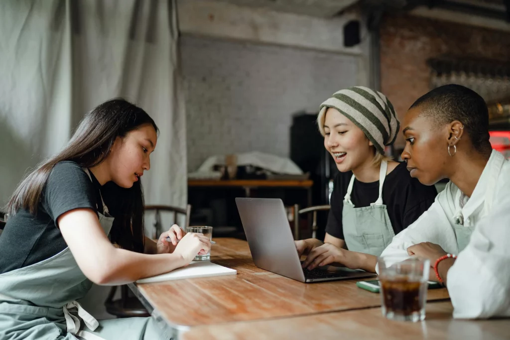 three co-workers sitting together at a laptop taking notes